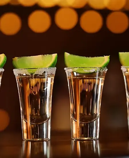 Vaso Shot conb tequila y un limón sobre mesa y fondo oscuro