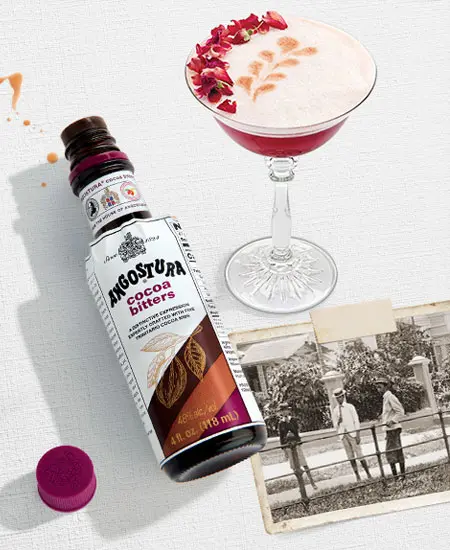 Angostura Cocoa (Esencias de gotas amargas) x 100ml junto a coctel rojo y fotografia antigua sobre mesa blanca