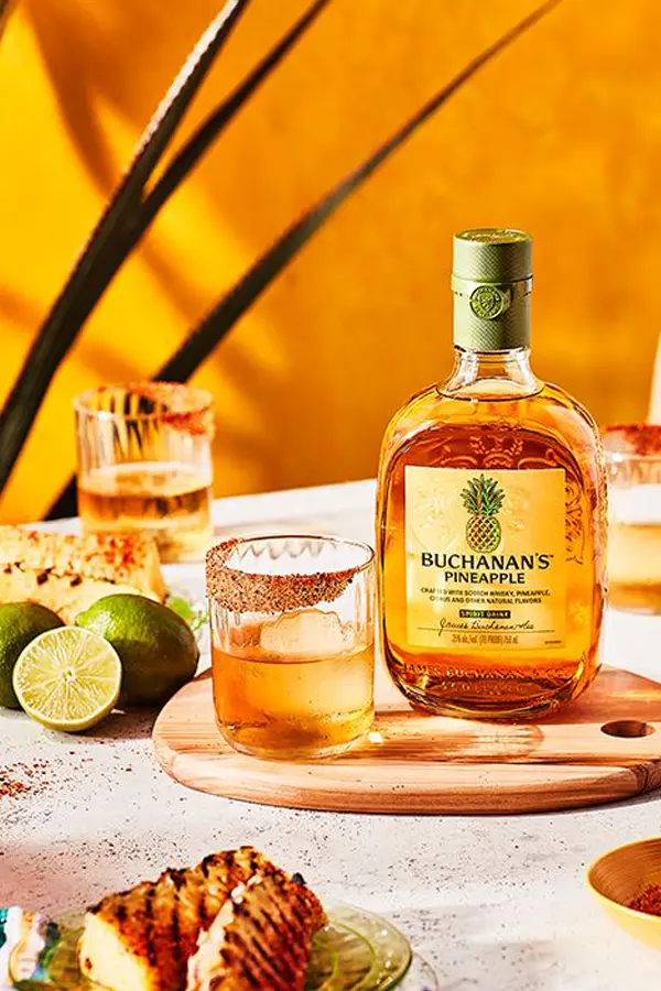 Buchanan's Pineapple x 750ml en mesa con dos copas con hielo y fondo amarillo